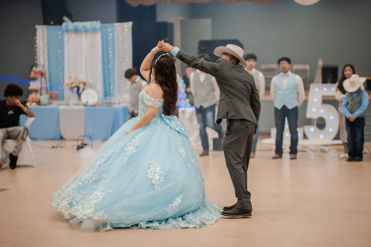 A young girl in a blue gown dances with a partner at a quinceañera celebration indoors.